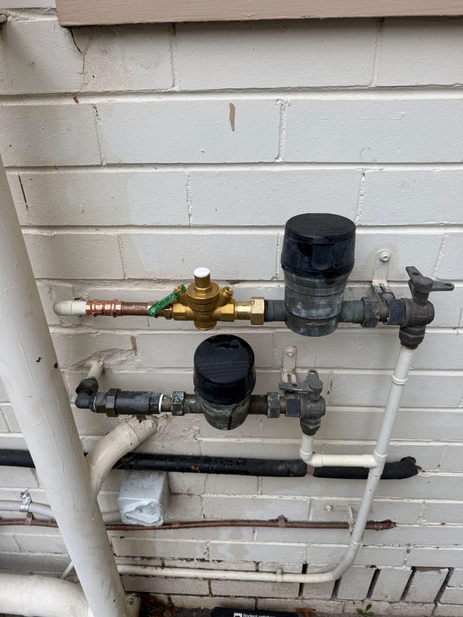 New brass pressure limiting valve and water meters installed on white brick wall Cheltenham Melbourne